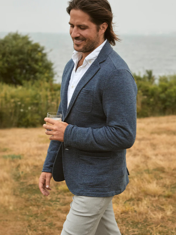 a man wearing a navy knit blazer over a collared shirt and slim fit pants