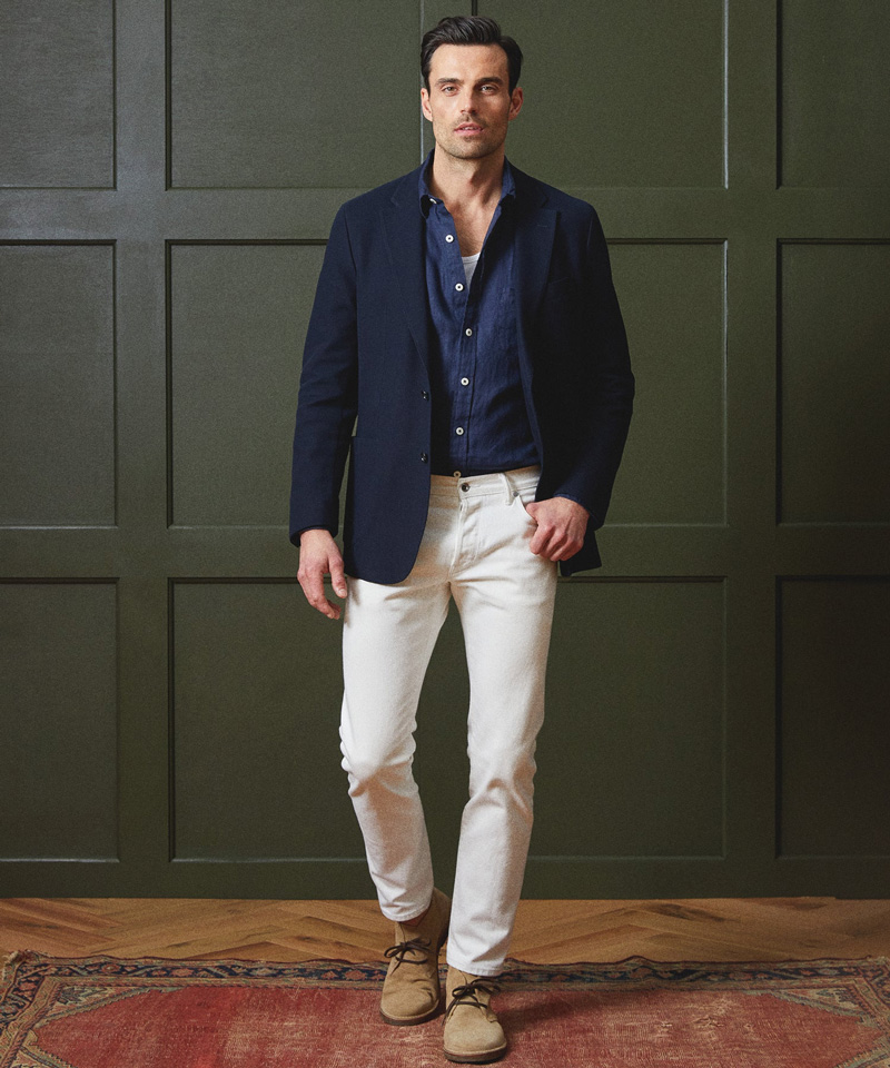 a man wearing a navy blazer, button up shirt, white pants, and lace up shoes