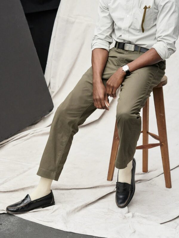 man sitting on a wooden stool wearing chino pants and loafer shoes