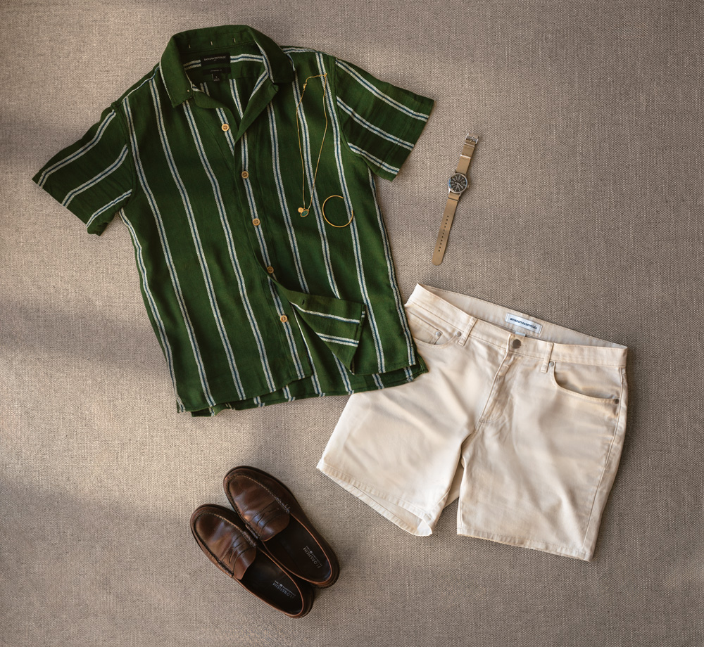 flat lay of men's summer outfit with green camp collar shirt, beige shorts, brown penny loaferes, field watch, gold necklace and gold bracelet