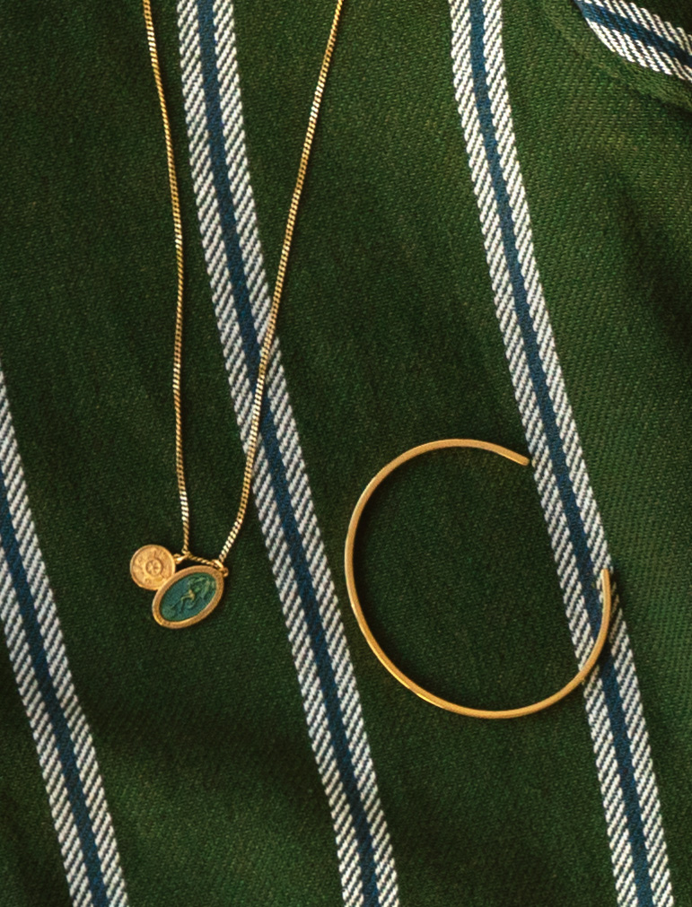 close up of a necklace and gold cuff on a green striped shirt