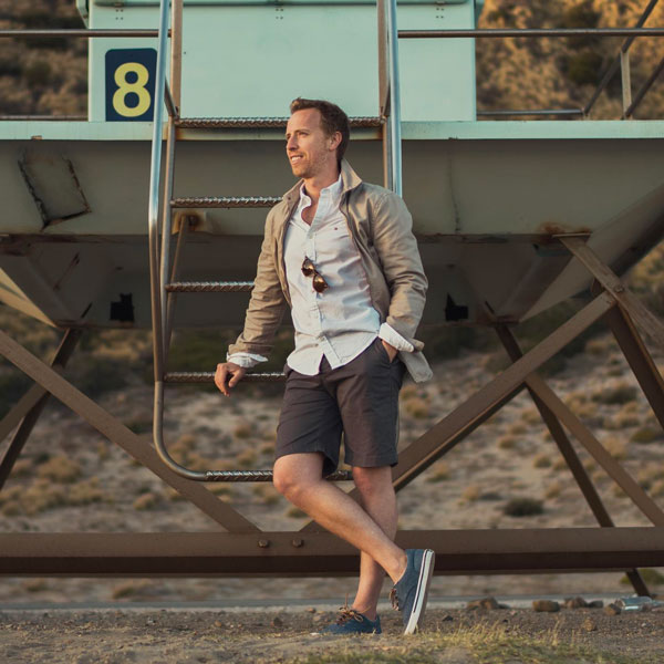 a man wearing a casual jacket over a button up shirt, shorts, and low top sneakers