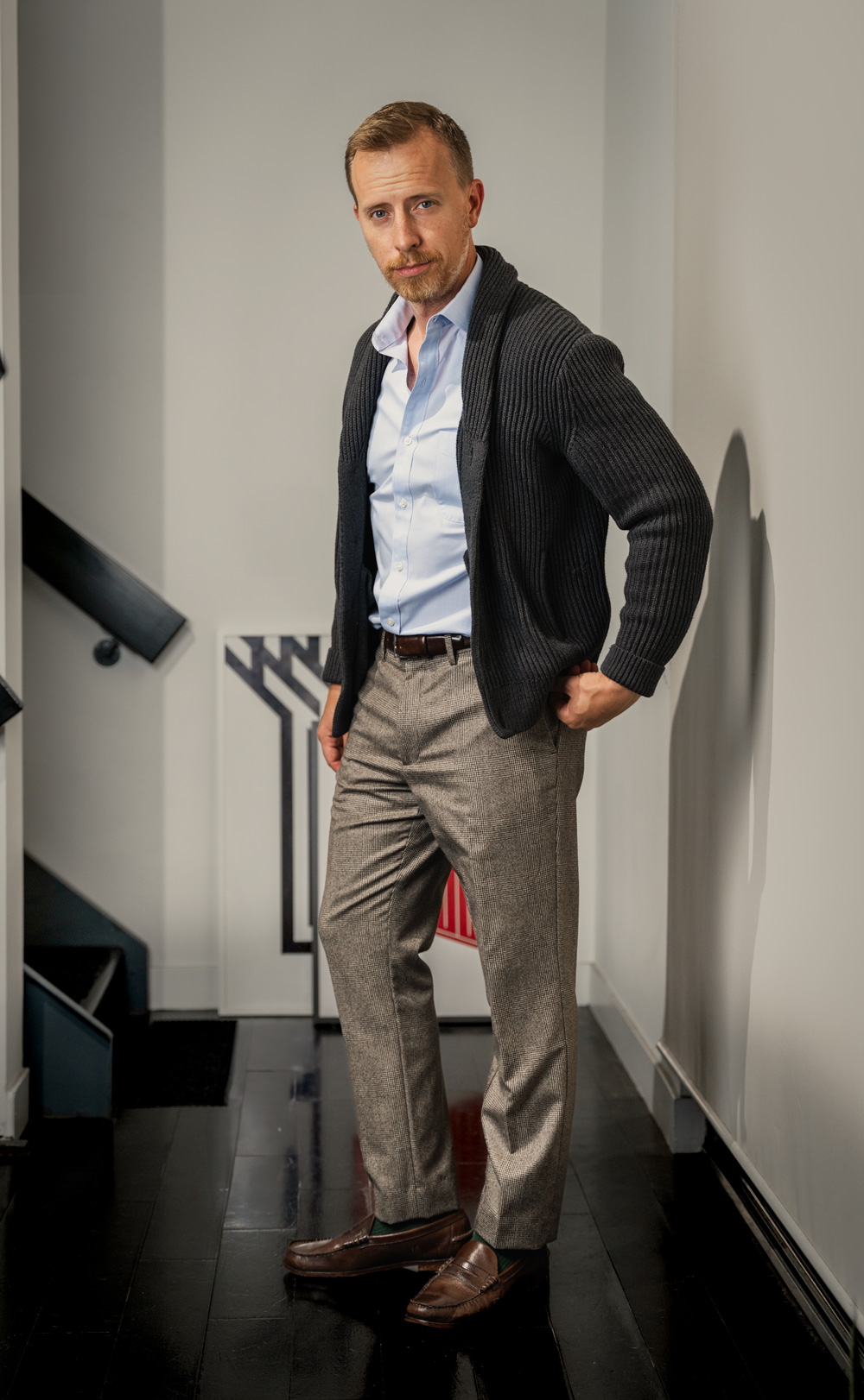 man wearing a fall business casual outfit featuring a grey shawl collar cardigan, blue dress shirt, tan dress pants, and penny loafers