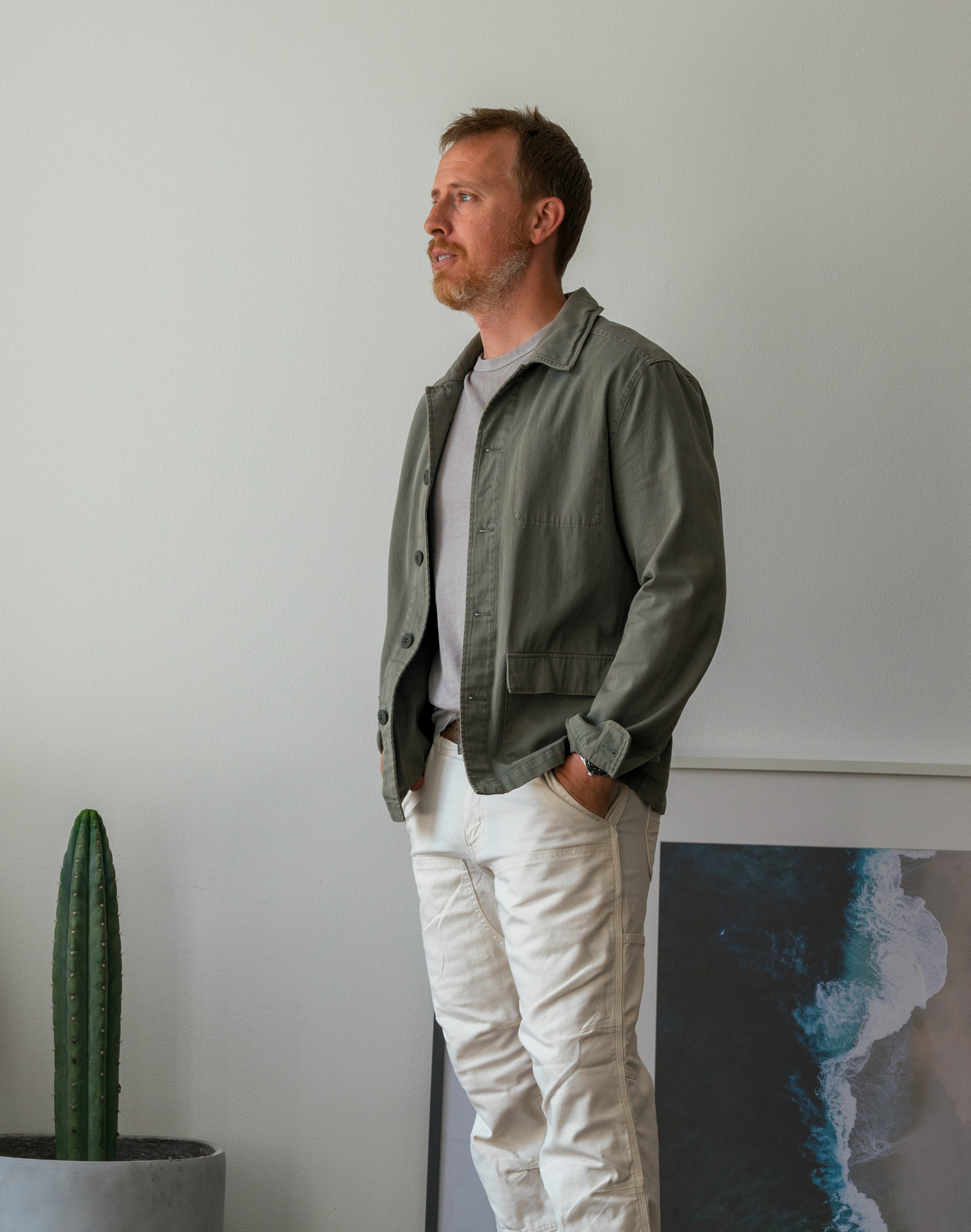 an olive chore coat worn with a gray t-shirt and white carhartt utility pants