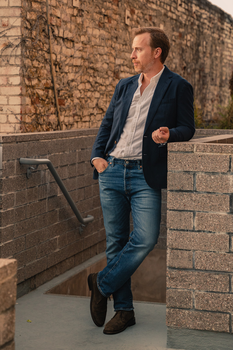 andrew snavely wearing a navy blazer over white oxford shirt, medium wash jeans, and suede chukka boots displaying a smart casual outfit