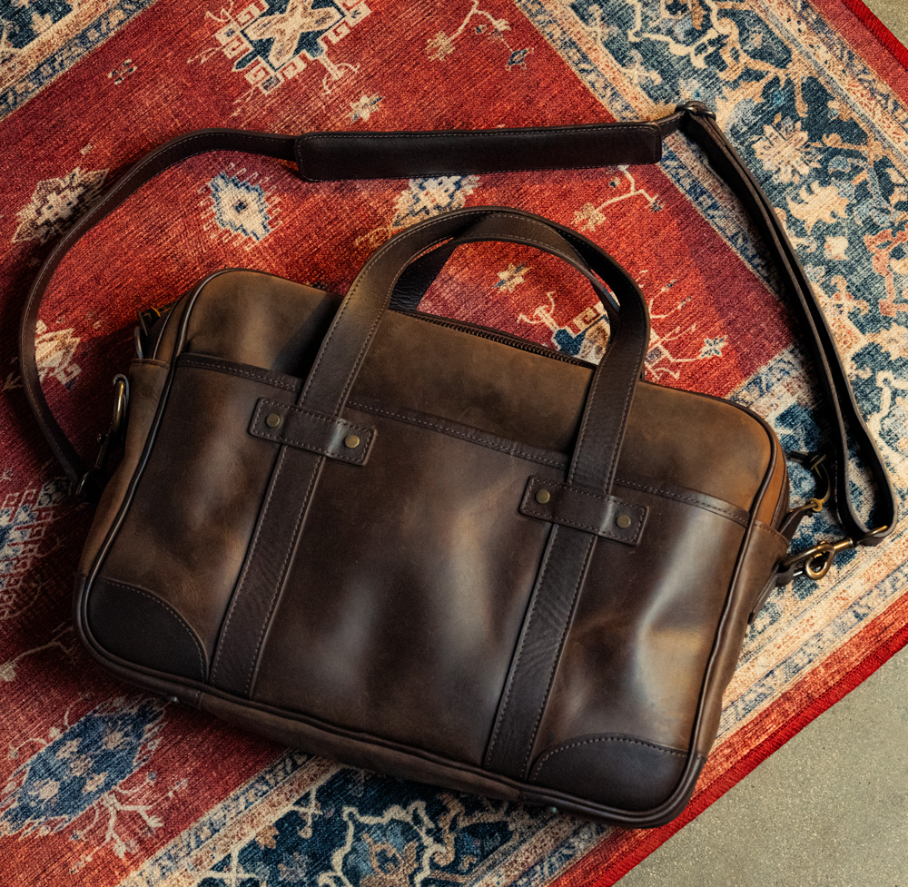 a brown thursday boot co leather messenger bag on an ornate red rug