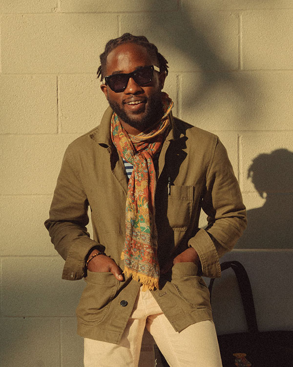 man wearing sunglasses, olive chore coat, and orange floral scarf