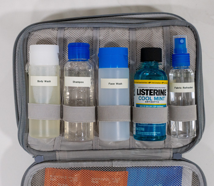 5 travel sized bottles in a travel case that read body wash, shampoo, face wash, LIsterine, and fabric refresher
