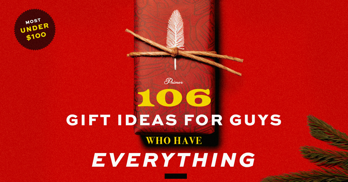 text "106 GIFT IDEAS FOR GUYS WHO HAVE EVERYTHING" in large, bold white and yellow letters against a vibrant red background. A stylized gift wrapped in red paper with a black pattern and the number "106" in yellow is tied with brown twine and a white feather. In the top left corner is a black starburst label with "MOST UNDER $100" in yellow, and a small green pine branch lies to the right of the gift. The text "Primer" appears at the bottom of the "106" on the gift.