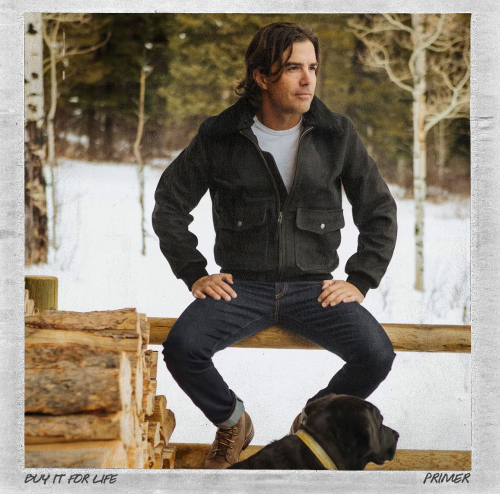 man wearing black nubuck bomber jacket while sitting on a fence post in winter
