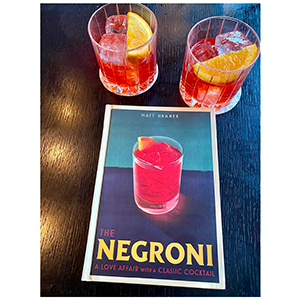 A signed copy of the book The Negroni: A Love Affair with a Classic Cocktail and two negroni beverages