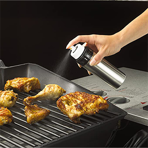 a brushed aluminum oil sprayer can being used to spray oil on food on a grill