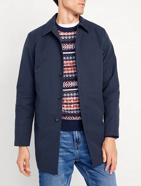 a man wearing a button front topcoat over a printed sweater and denim jeans