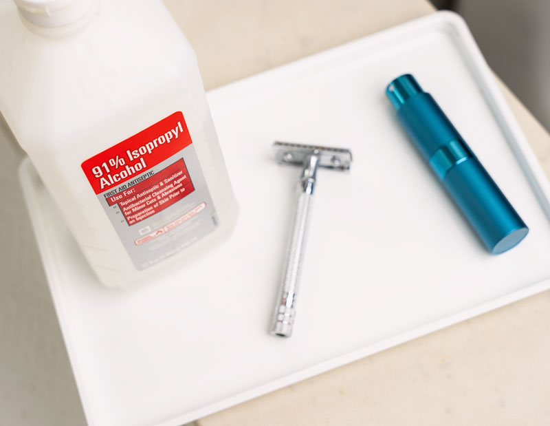 bathroom counter with a tray with rubbing alcohol, safety razor, and small mister bottle