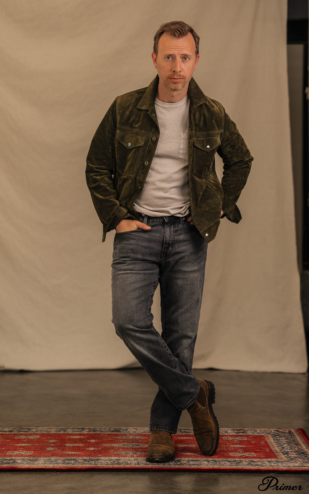 men's casual look with an olive green suede trucker jacket, a light gray pocket t-shirt, faded black jeans and brown chelsea boots