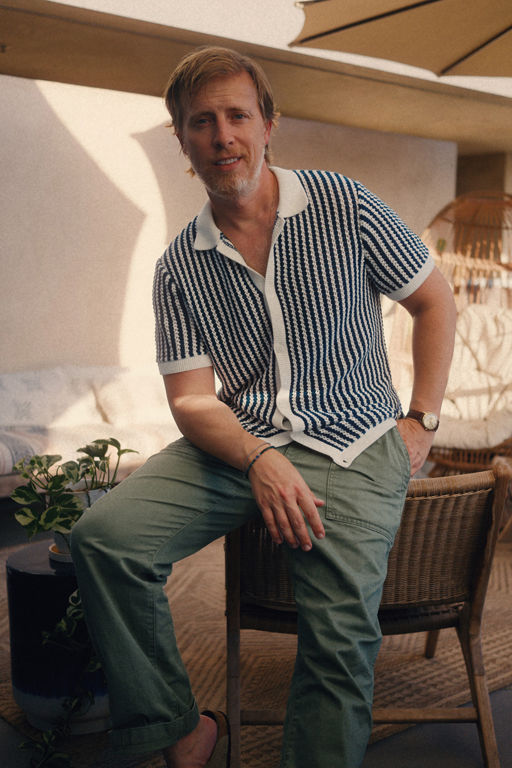 Men’s summer outfit featuring a blue and white striped casual knit polo with olive green utility og107 fatigue pants, styled on a hot sunlit patio.