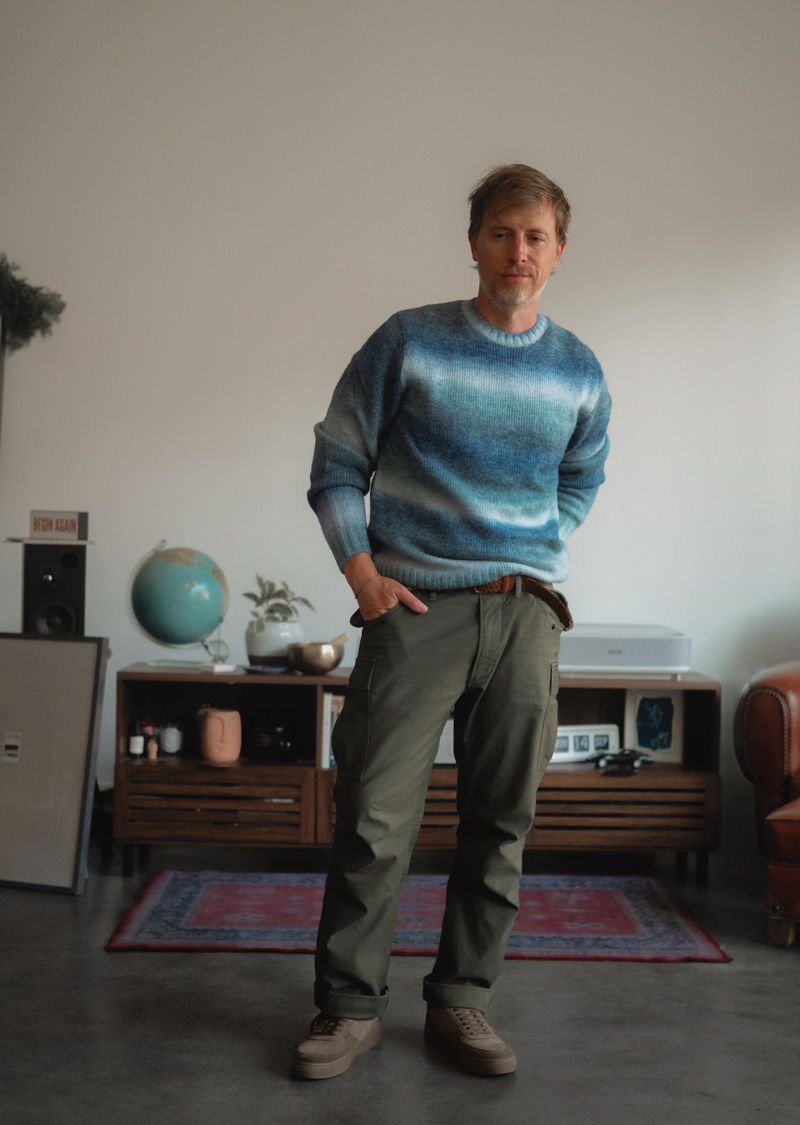 Man in a blue ombre striped Levi's crewneck sweater with olive pants and brown suede sneakers