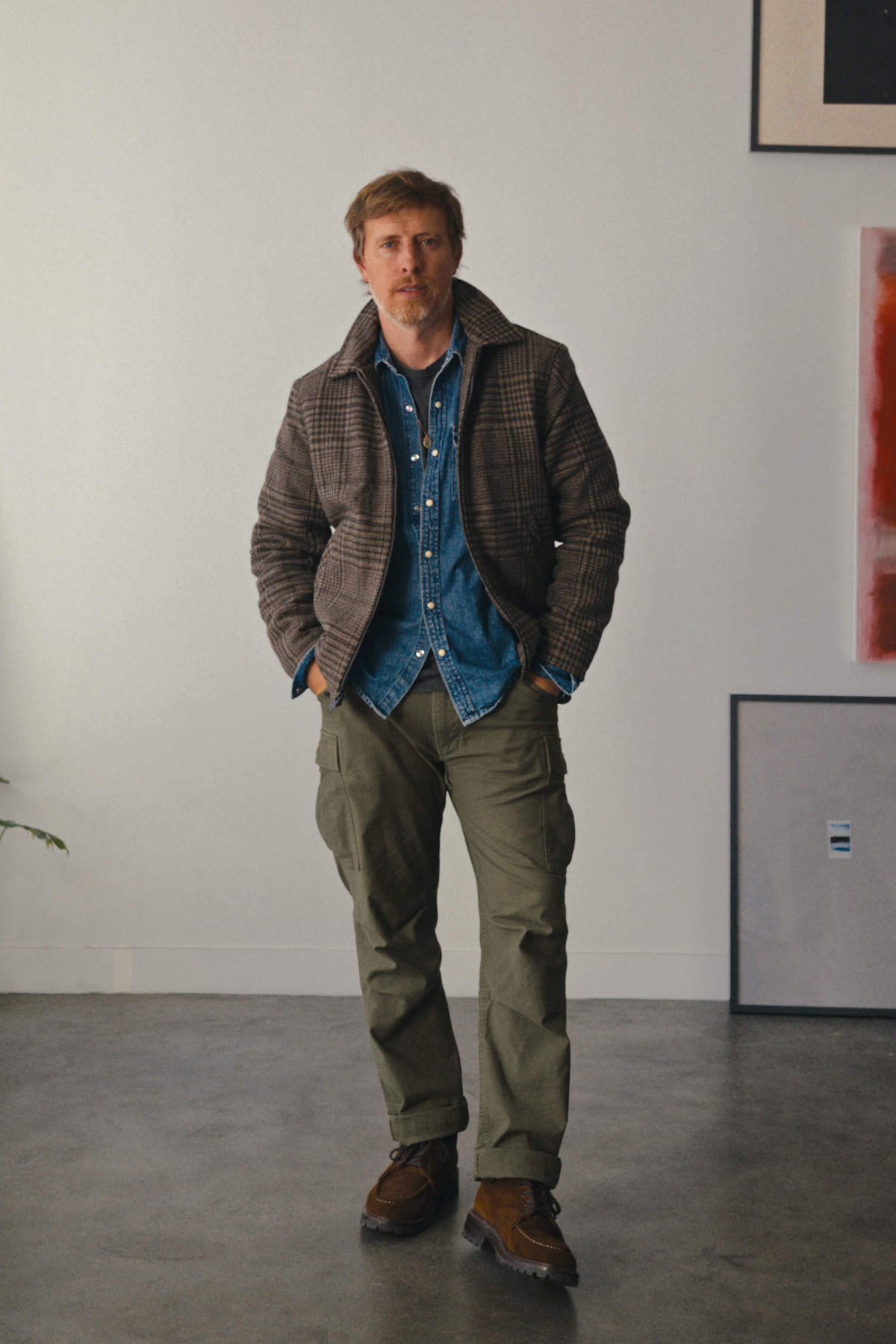 Man in a brown glen plaid Thursday Station Jacket over a denim shirt with olive cargo pants and brown moc toe boots